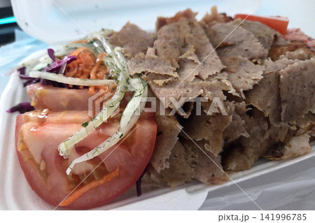 Sliced meat platter with fresh vegetables including tomatoes, cabbage, and onions served in a white takeout container on a table Sliced meat platter with fresh vegetables including tomatoes, cabbage, and onions served in a white takeout container on a table 141996785