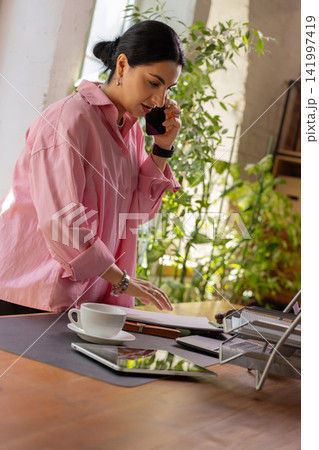 Professional woman handling phone call while working at office desk 141997419