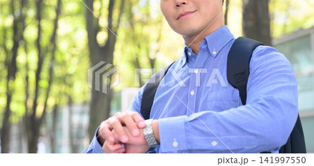 男性がリュックを背負い、腕時計を確認している様子 男性がリュックを背負い、腕時計を確認している様子 141997550