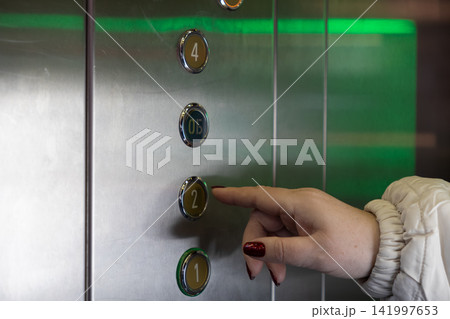 A person presses the elevator button for the second floor inside a modern building, illustrating daily urban commutes, vertical transport access, and simple routine travel navigation A person presses the elevator button for the second floor inside a modern building, illustrating daily urban commutes, vertical transport access, and simple routine travel navigation 141997653
