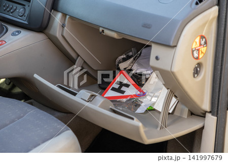 An open vehicle glove compartment filled with various items like a learner driver sign, representing messy car storage, clutter, maintenance preparation, and daily travel needs An open vehicle glove compartment filled with various items like a learner driver sign, representing messy car storage, clutter, maintenance preparation, and daily travel needs 141997679