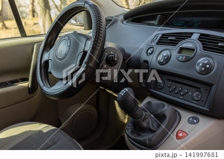Modern vehicle interior featuring a black leather steering wheel and manual gear stick in the center console, representing automotive design and a driver perspective on city travel Modern vehicle interior featuring a black leather steering wheel and manual gear stick in the center console, representing automotive design and a driver perspective on city travel 141997681