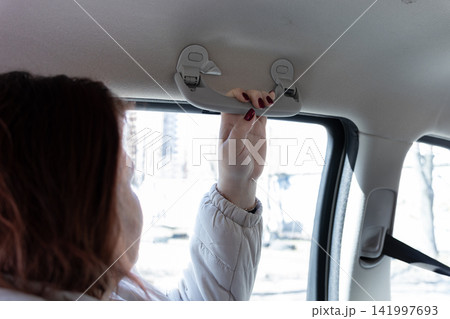 Passenger holding onto the grab handle inside a moving car, representing safety and support during a commute while sitting in the back seat with a calm and secure travel experience Passenger holding onto the grab handle inside a moving car, representing safety and support during a commute while sitting in the back seat with a calm and secure travel experience 141997693