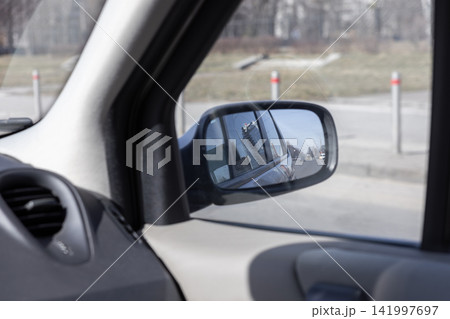 Side mirror reflection of a city building and urban road viewed from inside a parked car, conveying a sense of transition and travel while capturing everyday transit atmosphere Side mirror reflection of a city building and urban road viewed from inside a parked car, conveying a sense of transition and travel while capturing everyday transit atmosphere 141997697