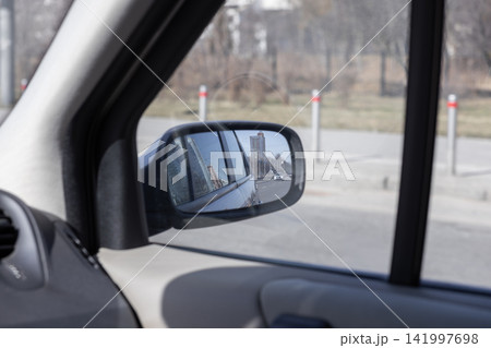 A car side mirror showing a cityscape reflection during a drive on an urban road, capturing a realistic perspective of modern transport and commuting through vehicle window glass A car side mirror showing a cityscape reflection during a drive on an urban road, capturing a realistic perspective of modern transport and commuting through vehicle window glass 141997698