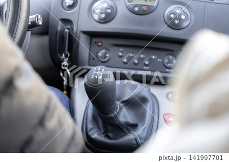 A manual gear shift lever sits inside a modern vehicle interior with dashboard controls visible in the background to illustrate the driving experience and mechanical operation A manual gear shift lever sits inside a modern vehicle interior with dashboard controls visible in the background to illustrate the driving experience and mechanical operation 141997701