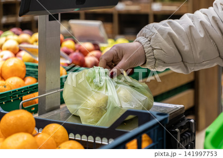 Person weighing a plastic produce bag of fresh fruit on a store scale, highlighting the routine shopping process in a grocery market setting for healthy food and retail convenience 141997753