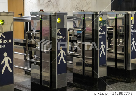 Metal turnstiles with exit signage lined up in a modern subway station, reflecting efficient passenger flow management in public transport infrastructure and urban commuter systems 141997773