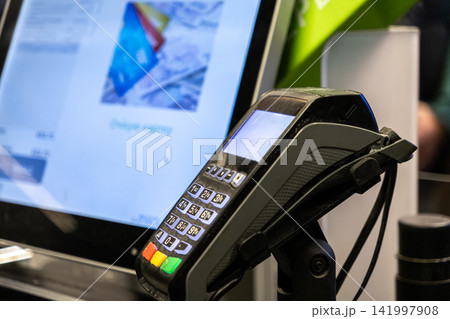 An electronic card payment terminal stands at a modern retail checkout desk near a digital display, representing secure transaction technology for fast commerce and business needs 141997908