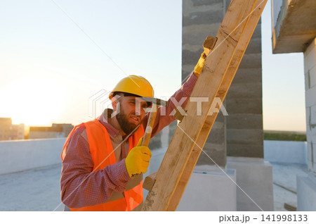 Construction worker building wooden structure on rooftop at sunset Construction worker building wooden structure on rooftop at sunset 141998133