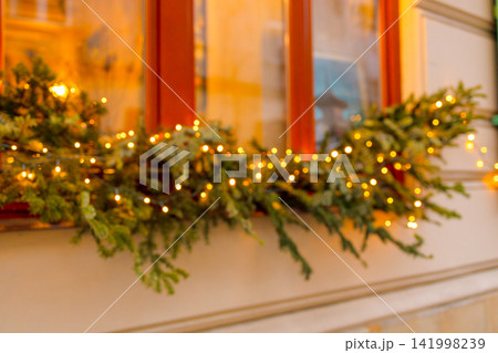 Cozy Christmas window display decorated with glowing lights and garland Cozy Christmas window display decorated with glowing lights and garland 141998239