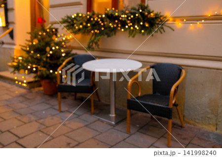 Empty cozy outdoor cafe terrace decorated with Christmas lights at evening Empty cozy outdoor cafe terrace decorated with Christmas lights at evening 141998240