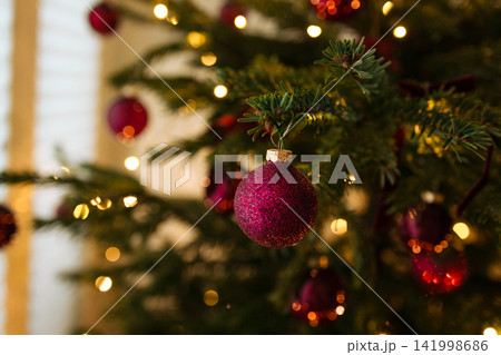 Purple glitter Christmas ornament on tree branch with warm bokeh lights Purple glitter Christmas ornament on tree branch with warm bokeh lights 141998686