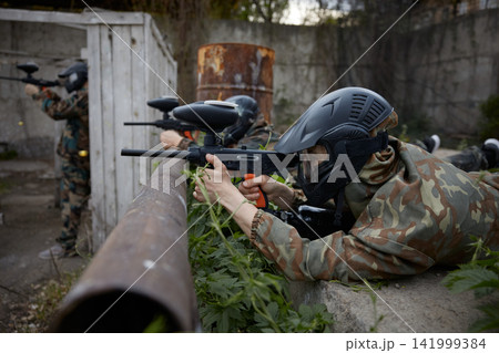 Portrait of a soldier aims a gun while leaning on a pipe, lying on the ground Portrait of a soldier aims a gun while leaning on a pipe, lying on the ground 141999384