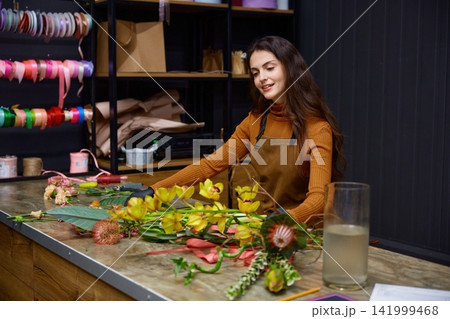 Dedicated flower artisan designs colorful bouquets diligently within cozy studio 141999468