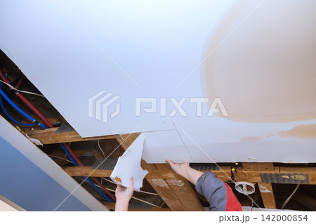Builder is seen working on installing drywall in residential space pipes, wires are above ceiling. 142000854