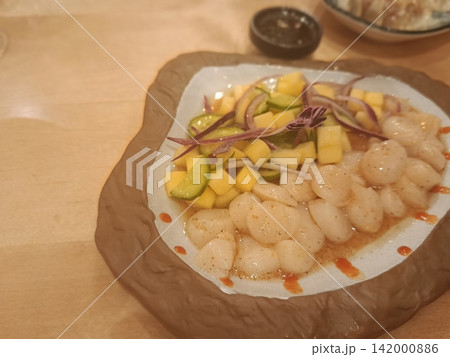 Scallop crudo with fresh mango salsa, sliced cucumber, and red onion, representing a gourmet seafood appetizer in a restaurant setting 142000886
