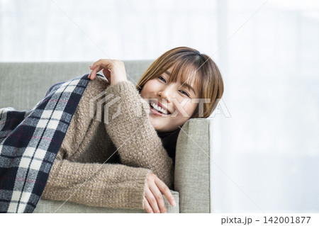 ストールを掛けてソファーに横になる若い女性 ストールを掛けてソファーに横になる若い女性 142001877