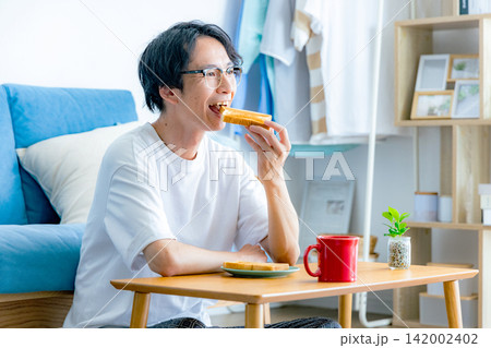 朝ごはんのトーストを食べる若い男性 142002402