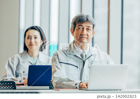 作業着姿でオフィスでノートパソコンを使う60代男性社員 作業着姿でオフィスでノートパソコンを使う60代男性社員 142002823