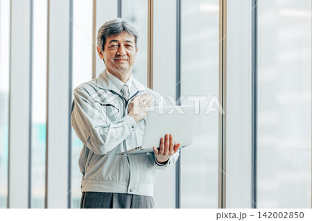 作業着姿でノートパソコンを持つシニア男性技術者 作業着姿でノートパソコンを持つシニア男性技術者 142002850