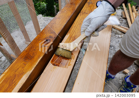 Worker applying wood stain to wooden boards with a brush Worker applying wood stain to wooden boards with a brush 142003095