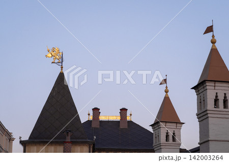 Historic building rooftops display ornate spires and a golden weather vane, set against a clear evening sky with soft lighting 142003264