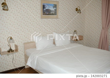 Modern bedroom features a double bed with white linens, decorative wall art above, and stylish bedside lamps against floral wallpaper Modern bedroom features a double bed with white linens, decorative wall art above, and stylish bedside lamps against floral wallpaper 142003271