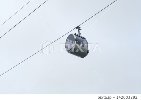 Aerial gondola cabin hangs from cables in the sky, highlighting contemporary transport design against a backdrop of gray clouds Aerial gondola cabin hangs from cables in the sky, highlighting contemporary transport design against a backdrop of gray clouds 142003292