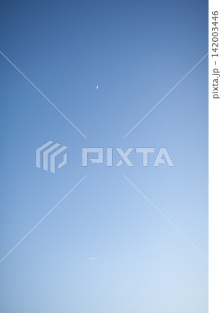 Crescent moon appears in a clear blue sky at twilight, accompanied by a faint contrail from an airplane, creating a serene atmosphere Crescent moon appears in a clear blue sky at twilight, accompanied by a faint contrail from an airplane, creating a serene atmosphere 142003446