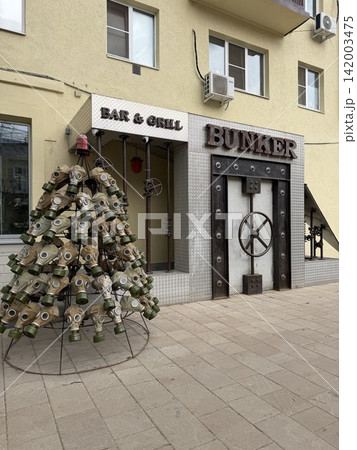 Ryazan, Russia - April 06, 2026: Entrance of a bar and grill featuring a bunker-style door and a tree made of gas masks in an urban environment Ryazan, Russia - April 06, 2026: Entrance of a bar and grill featuring a bunker-style door and a tree made of gas masks in an urban environment 142003475