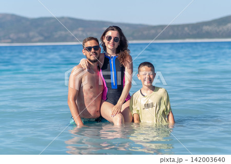 A family of three relaxes in calm, clear water at the beach. A family of three relaxes in calm, clear water at the beach. 142003640