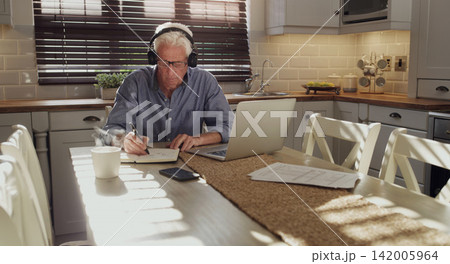 Computer, writing and senior man with headphones in home planning retirement fund, finance or saving. Technology, notebook and person with laptop for online mortgage, debt or bills payment in kitchen 142005964