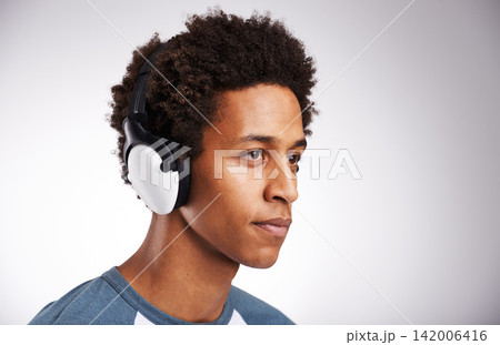 Young man, headphones and listening with music for podcast or audio streaming on a gray studio background. Face of male person, model and earphones for radio, sound or entertainment on mockup space 142006416