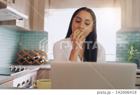Kitchen, apple and woman with laptop for remote work, breakfast and coffee for online career. Eating fruit, reading and freelancer girl in home with computer for web project, research and nutrition. 142006419