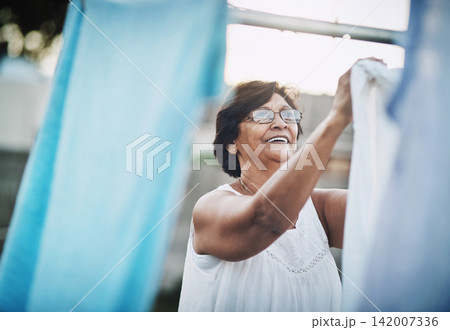 Mature woman, clothesline and laundry in garden with household domestic chores, spring cleaning and housekeeping. Hanging clothes, fabric or white cotton sheet, cleaner and housework outdoor Mature woman, clothesline and laundry in garden with household domestic chores, spring cleaning and housekeeping. Hanging clothes, fabric or white cotton sheet, cleaner and housework outdoor 142007336
