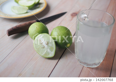 Slicing limes beside a glass of lime drink on wooden table Slicing limes beside a glass of lime drink on wooden table 142007768