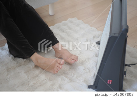 Bare Feet Warming by a Space Heater on a Cozy Rug in a Living Room 142007808