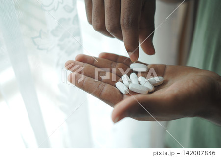 Hands hold white tablets near a window 142007836