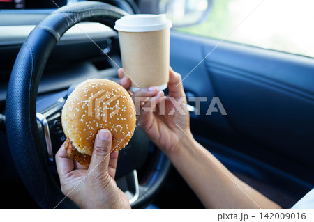 Asian woman driver hold and eat hamburger food in car. Asian woman driver hold and eat hamburger food in car. 142009016