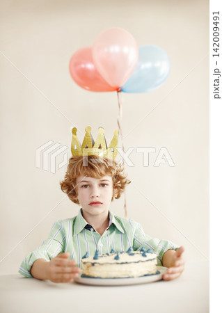 Birthday cake, portrait and balloons with sad boy by table in family home for celebration, growth and lonely. Dessert, decoration and sweet pastry for event, serious and milestone with crown in house Birthday cake, portrait and balloons with sad boy by table in family home for celebration, growth and lonely. Dessert, decoration and sweet pastry for event, serious and milestone with crown in house 142009491