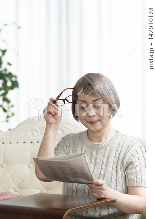 リビングで老眼鏡をかけて新聞を読むシニア女性 142010178