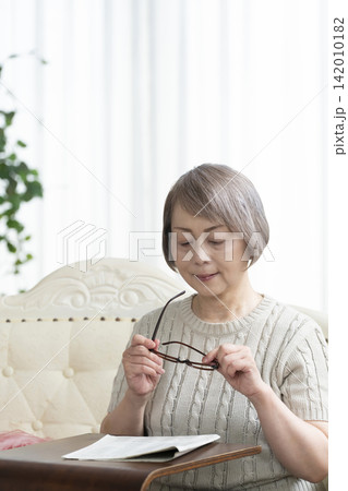 リビングで老眼鏡をかけて新聞を読むシニア女性 リビングで老眼鏡をかけて新聞を読むシニア女性 142010182