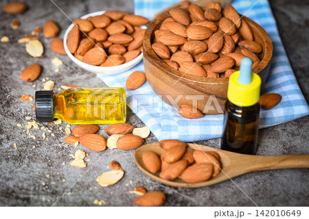 Almond oil and Almonds nuts on bowl dark background, Delicious sweet almonds oil in glass bottle, roasted almond nut for healthy food and snack organic vegetable oils for cooking or spa Almond oil and Almonds nuts on bowl dark background, Delicious sweet almonds oil in glass bottle, roasted almond nut for healthy food and snack organic vegetable oils for cooking or spa 142010649