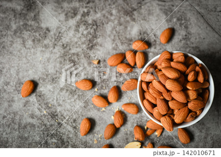 Almonds nuts on white bowl, Delicious sweet almonds on the table dark background, roasted almond nut for healthy food and snack 142010671