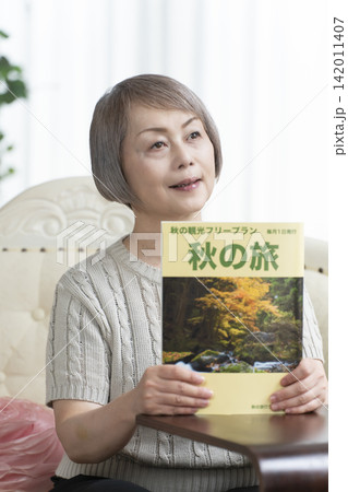 リビングのソファーで旅行雑誌を見るシニア女性 リビングのソファーで旅行雑誌を見るシニア女性 142011407