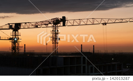 Construction cranes silhouetted against a vibrant sunset sky Construction cranes silhouetted against a vibrant sunset sky 142013287