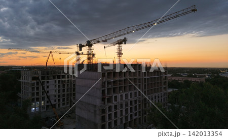 Construction site with cranes and unfinished buildings at sunset Construction site with cranes and unfinished buildings at sunset 142013354