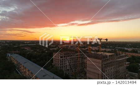 Construction site at sunset with cranes and city skyline in view Construction site at sunset with cranes and city skyline in view 142013494
