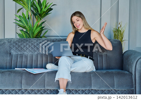 Young woman talking and gesturing during online video call on laptop sitting on sofa at home 142013612